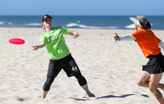 Woman playing ultimate frisbee barefoot on the beach in a state of flow, fully recovered after injury—symbolizing presence over pressure in peak performance.