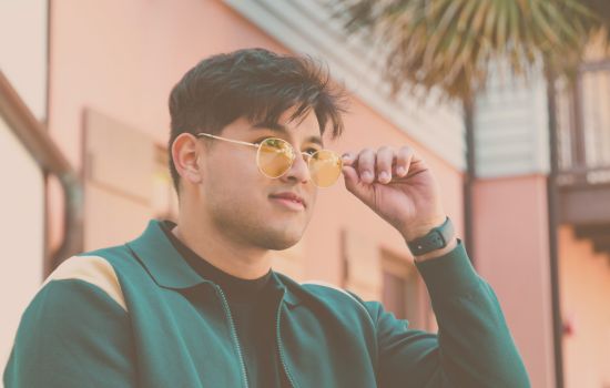 Young man outdoors wearing stylish yellow-tinted blue light blocking glasses, adjusting his frames in natural daylight.
